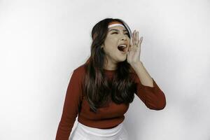 Young beautiful woman wearing a red top shouting and screaming loud with a hand on her mouth. Indonesia's independence day concept. photo