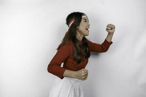 A young Asian woman with a happy successful expression wearing red top and flag headband isolated by white background. Indonesia's independence day concept. photo