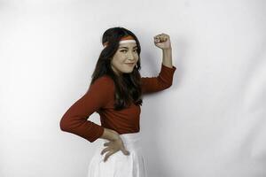 A young Asian woman with a happy successful expression wearing red top and flag headband isolated by white background. Indonesia's independence day concept. photo