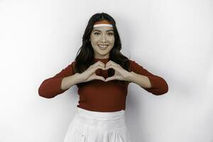 A young Asian woman wearing a red top feels nationalism, shapes heart gesture expresses her love for Indonesia. Indonesia's independence day concept. photo