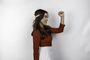 A young Asian woman with a happy successful expression wearing red top and flag headband isolated by white background. Indonesia's independence day concept. photo