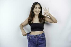dieta y peso pérdida concepto. un joven asiático mujer en de gran tamaño pantalones aislado en un blanco antecedentes. foto