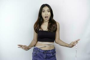 Diet lifestyle concept. Shocked Asian girl measuring her waist with measuring tape, isolated by white background photo