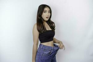 Diet and weight loss concept. A young Asian woman in oversized jeans isolated on a white background. photo