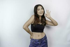 Portrait of happy young Asian woman wearing crop top showing approval gesture with her fingers, isolated over white background. Diet concept. photo