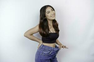 Diet and weight loss concept. A young Asian woman in oversized jeans isolated on a white background. photo