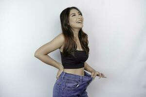 Diet and weight loss concept. A young Asian woman in oversized jeans isolated on a white background. photo