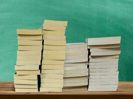 A pile of books laying on a wooden table with a green board in the background. photo