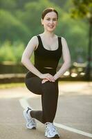 retrato de sonriente joven mujer en negro ropa de deporte hacer ejercicio al aire libre. aptitud y sano estilo de vida concepto. foto