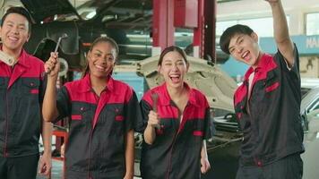 Multiracial professional mechanic workers team after work celebrating automotive repair jobs success, hand raises with fixing tools with cheerful smiles and look at camera at a service car garage. video