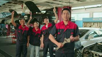 gracioso retrato de profesional trabajadores equipo, masculino supervisor brazos cruzado con fijación herramientas en frente de mecánico colegas, celebra coche reparar trabajos éxito con alegre sonrisas a Servicio cochera. video