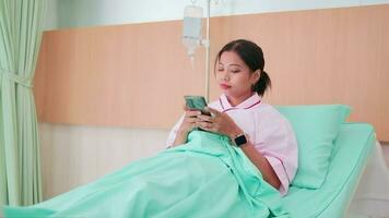 1 ásia fêmea paciente chats em social meios de comunicação Móvel telefone através da conectados tecnologia dentro hospital enfermaria paciente internado cama para recuperação resultados depois de cuidados de saúde exame e médico tratamento. video