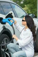 joven negocio mujer repostaje su eléctrico coche a un ev cargando estación. concepto de ambientalmente simpático vehículo. eléctrico coche concepto. verde de viaje. foto