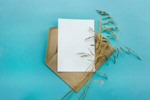 un Kraft papel sobre con un blanco blanco tarjeta flores en un azul antecedentes. tarjeta postal preparación foto
