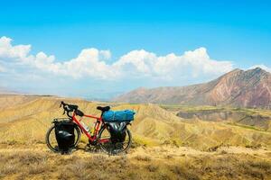 Loaded touring bicycle stands with moody dramatic panoramic mountains view and no cyclist photo