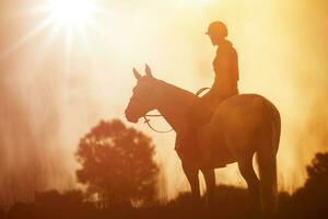 The silhouette of a horse rider and her horse against the background of sunset. photo