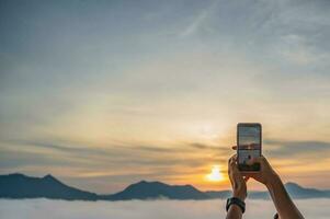 turista mano utilizar móvil teléfono tomar un foto de amanecer y mar de niebla en phu gracias a chiang kan en el temprano mañana.chiang kan es un antiguo pueblo y un muy popular destino para tailandés turistas