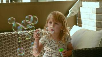 pequeño niña soplar jabón burbujas en el terraza sofá en Hora de verano video