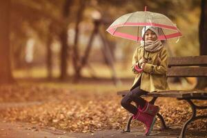 Little girl with an umbrella and a basket on a park bench photo