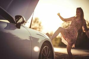 mujer pateando su roto coche. puesta de sol. foto