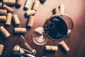 Red wine glass, corks and corkscrew on wooden table. photo