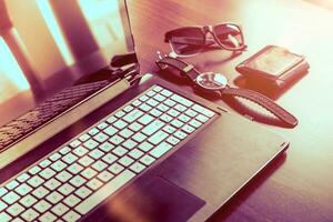 Laptop computer, watch, glasses and wallet on wooden desk photo