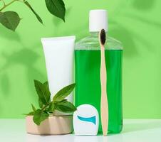 Refreshing mouthwash in a transparent plastic bottle and dental floss, white tube on a green background photo