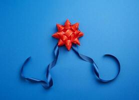 blue silk thin ribbon twisted and red shiny bow on a blue background photo