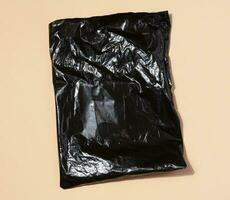 Black plastic bag on a beige background, top view photo