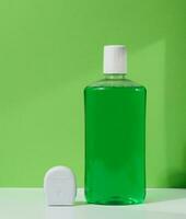 Refreshing mouthwash in a transparent plastic bottle and dental floss on a green background photo