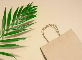 Empty disposable brown kraft paper bag with handles on beige background, eco packaging, zero waste photo