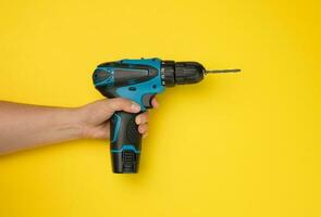 female hand holds a cordless drill on a yellow background. Tool for work photo