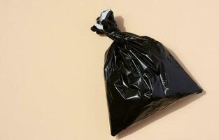 Full black plastic bag on a beige background, top view photo