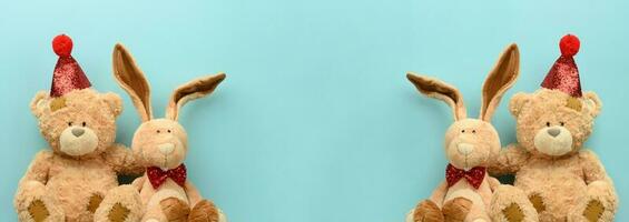 Teddy bear in a festive cap and a plush hare on a blue background. Festive background photo