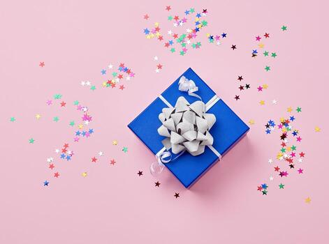 azul cartulina cuadrado caja atado arriba con un blanco cinta con un brillante arco y dispersado multicolor brillante en forma de estrella papel picado foto