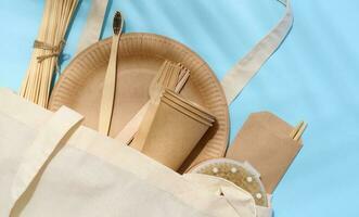 White cotton bag, wooden forks, plates and cups on a blue background. Waste recycling concept, zero waste photo