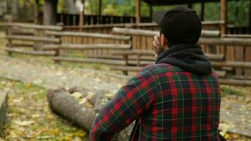 back view. Outdoor a man in a cap with a beard drinks Chinese tea from a bowl video