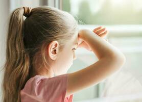 triste pequeño niña mirando mediante ventana a hogar. foto