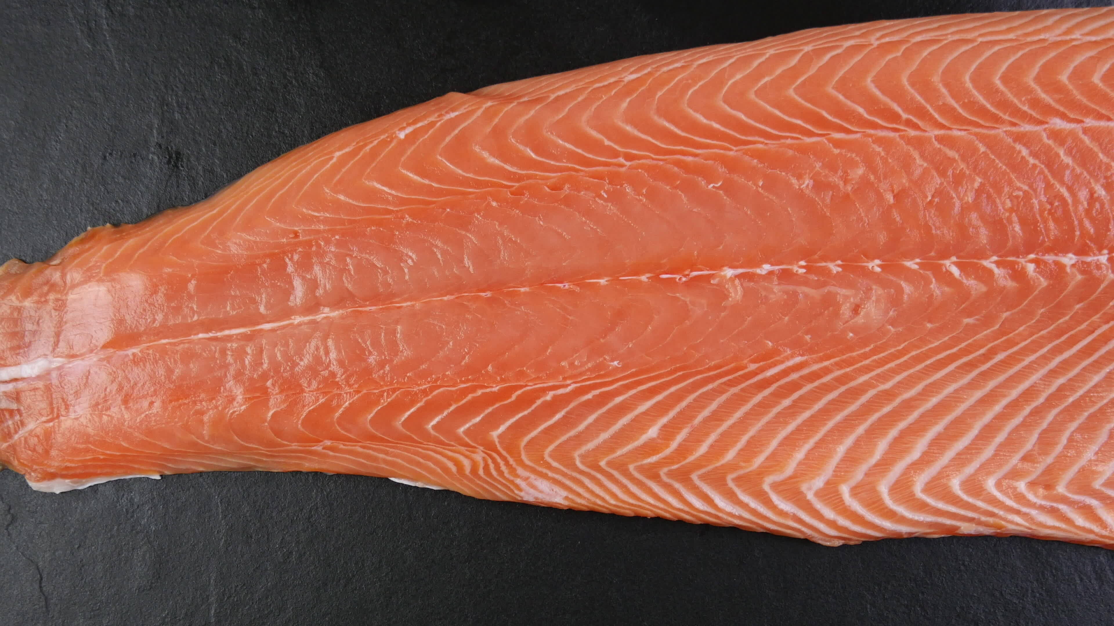 fresh raw salmon trout half body fillet over black stone surface, top