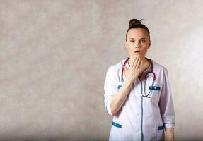 Young female doctor dressed in a white medical uniform has a scared expression of a face. photo