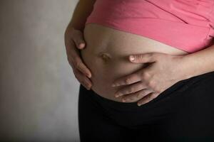 joven embarazada mujer toques su barriga. dramático ligero. foto