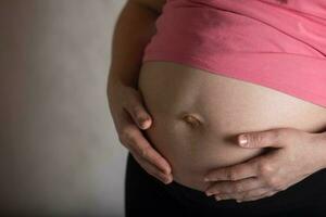 joven embarazada mujer toques su barriga. dramático ligero. foto