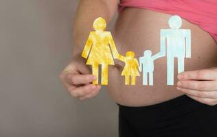 Young pregnant woman keeps paper cutouts of a family. Closeup photo