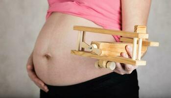 joven embarazada mujer mantiene de madera hecho avión. foto