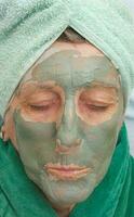 A senior's face is covered by clay facial mask.Close up photo
