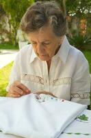 An old woman is embroidering on the white blanket photo