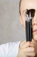 Young lady keeps make up brushes kit close to her face. Closeup photo