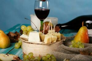 Cheese slices, pear, and grapes on a wooden stand. photo