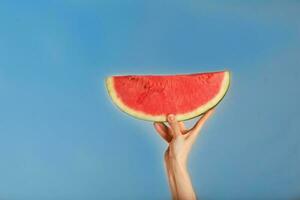 Young lady keeps a slice of water melon on a blue background. photo