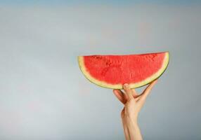 Young lady keeps a slice of water melon on a blue background. photo